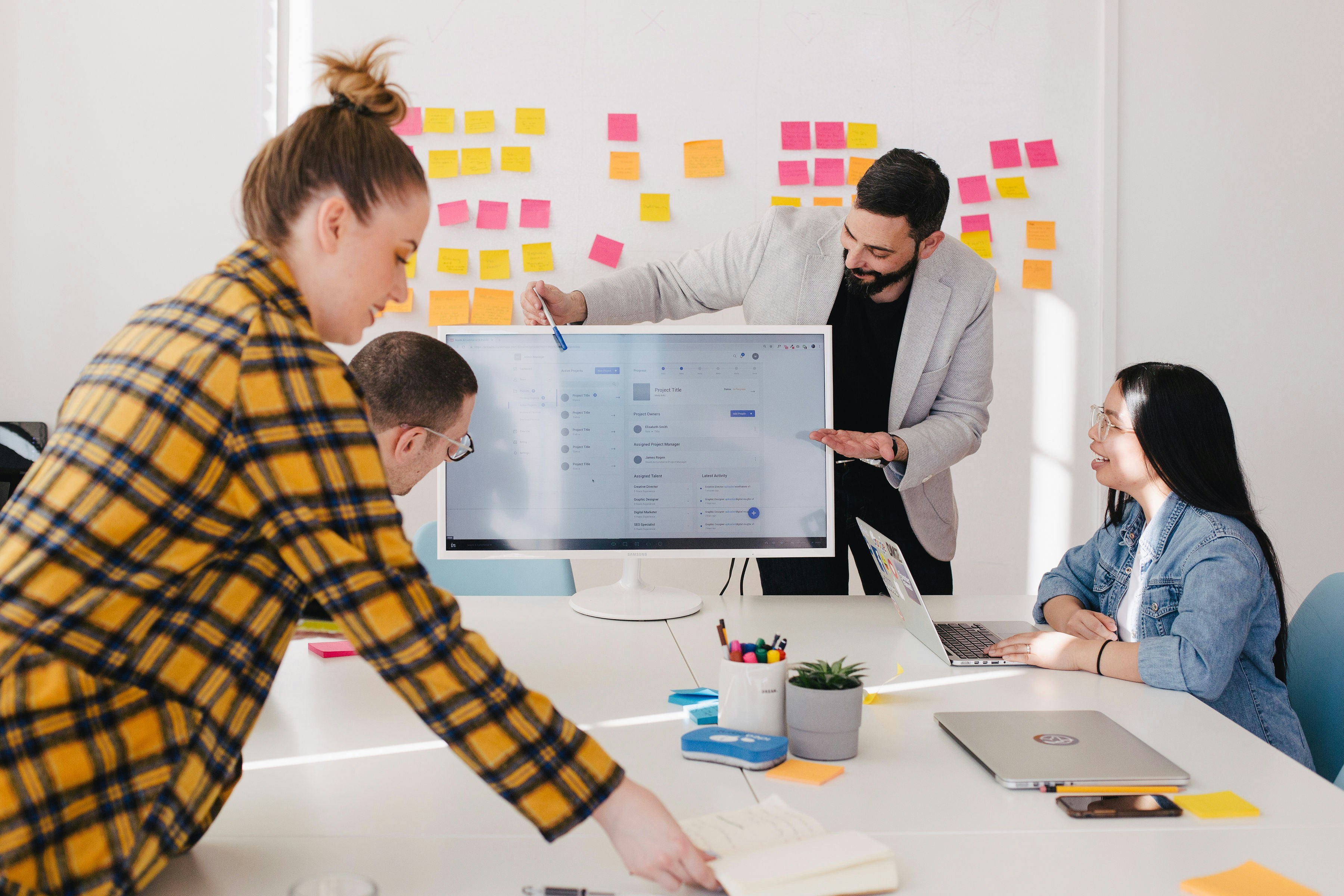 A team collaborating on training and documentation in a modern office, gathered around a large monitor displaying a digital interface.