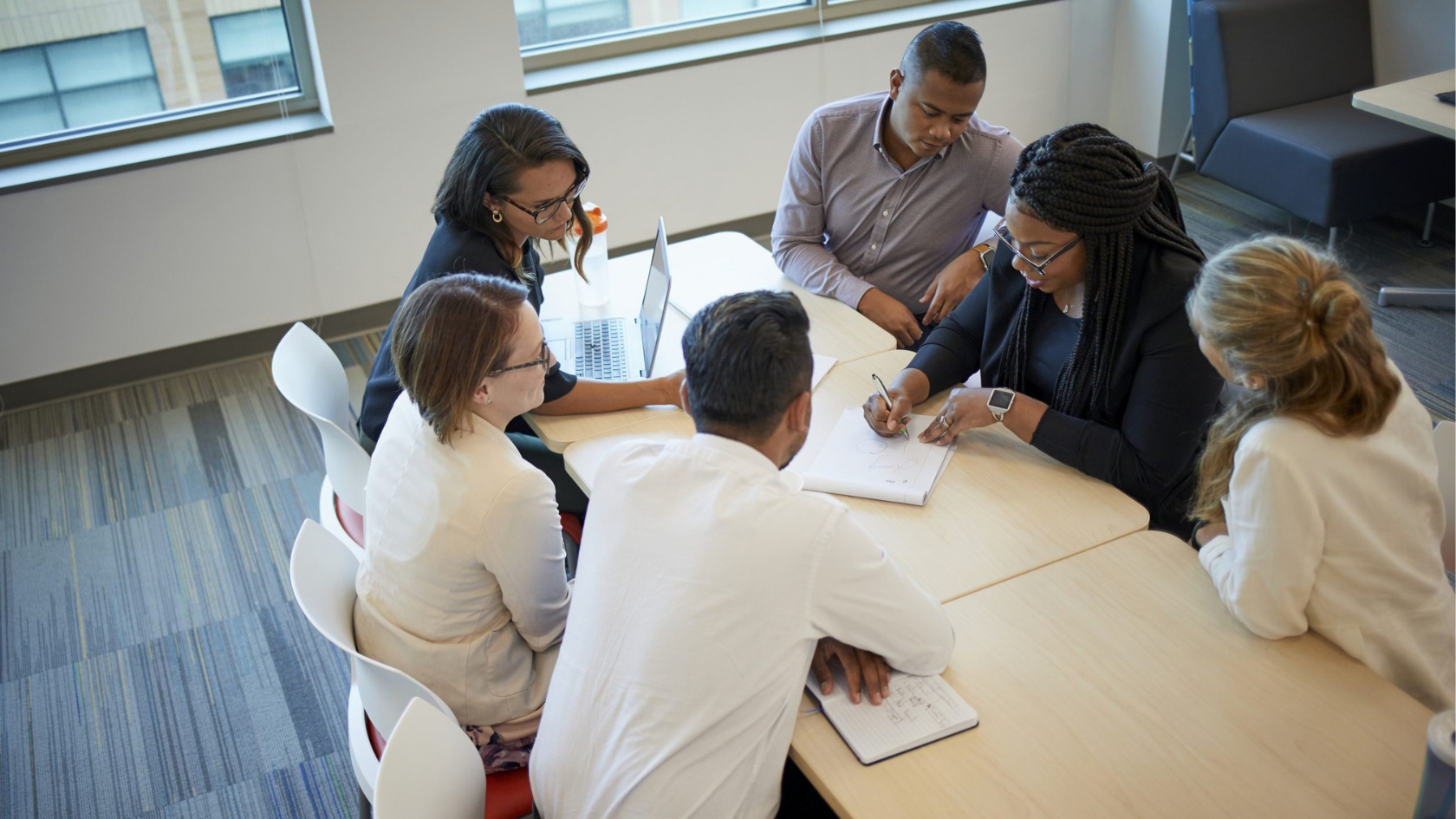 A diverse team of six professionals collaborating around a light wooden table in a bright, modern office.